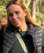 Kristen Buchanan smiling with long light brown hair and wearing a black vest over a long sleeve green top