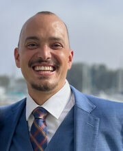 Dr. Aaron Coleman smiling with very short brown hair, mustache and goatee. He is wearing a blue blazer and vest over a white button down shirt with blue tie