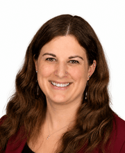 Dr. Michelle Commeret smiling with long wavy brown hair and wearing a  maroon blazer over a black top