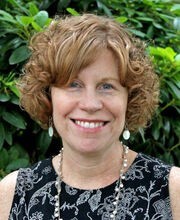 Diane Crowley smiling with medium length curly light brown hair and wearing a sleeveless black with white print top
