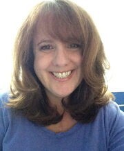 Sheila J. Gibbons smiling with long light brown wavy hair wearing a blue crew neck top