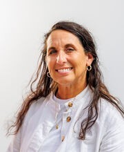 Tammy Greene smiling with long brown hair and wearing a white button up jacket over a white top