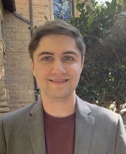 Dr. Ryan Hannagan smiling with short brown hair and wearing a grey blazer over a maroon shirt