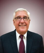 Dr. Mike Kryzanek smiling with short gray hair and wearing black rim glasses and a navy blue blazer over a white button down shirt and a dark red tie