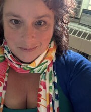 Bridget Lehane smiling with medium length curly brown hair and wearing a blue sweater and colorful scarf