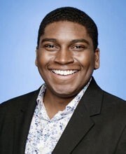 Dr. Niles Mattier smiling with short black hair and wearing a black blazer over a white and blue print button down shirt