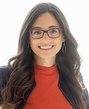 headshot photo of Dr. Michele Meek with long dark brown hair wearing brown rim glasses, a red top and black zipper up jacket