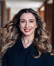 Patricia Morchel smiling with long wavy brown hair wearing a navy blue blazer with navy blue v-neck top under it
