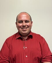 Dr. Matthew Moreau balding with very short dark brown hair smiling and wearing a red polo shirt