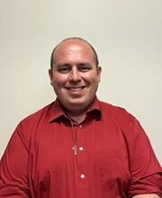 Dr. Matthew Moreau balding with very short dark brown hair smiling and wearing a red polo shirt
