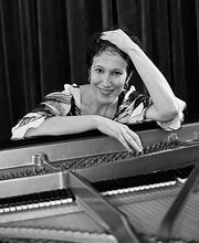 black and white photo of Dr. Deborah Nemko smiling at her piano with short dark brown hair