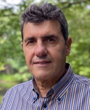 Dr. Simone Poliandri smiling with short wavy salt and pepper hair and wearing a blue, yellow and red striped button down shirt