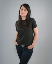 Colleen Kelly Poplin with long dark brown hair and wearing a black short sleeve top and black jeans