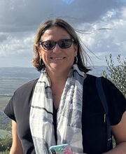 Dr. Gia Renaud smiling with medium length straight brown hair and wearing sunglasses, a short sleeve black top and a white and black scarf