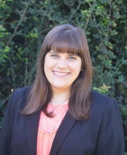 Dr. Brittany Russo smiling with long brown hair and wearing a navy blue blazer over a pink top