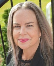 Ellen Scheible smiling with long straight gray hair and wearing a black blazer over a black top with lace in the neckline