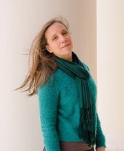 Jennifer Schoonover smiling standing next to a large white column on the portico of Boyden Hall with long straight light brown hair wearing a teal blue sweater and green scarf