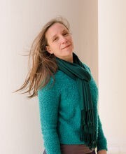 Jennifer Schoonover smiling standing next to a large white column on the portico of Boyden Hall with long straight light brown hair wearing a teal blue sweater and green scarf