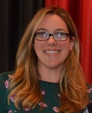 Dr. Melinda Tarsi-Goldfien smiling wearing black rim glasses, long dirty blonde wavy hair and a dark green top with pink floral pattern