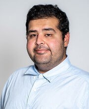 headshot of Dr. Waleed Jami with short wavy dark brown hair, mustache and goatee and wearing a light blue button down shirt