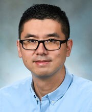 Dr. Eric Yao with short dark hair and wearing black rim glasses and a blue button down shirt
