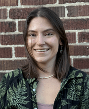 Dr. Mel Zarate smiling with medium length straight brown hair and wearing a black button down top with green print over a pink top