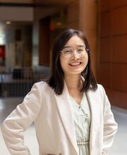 Dr. Hui Zhang smiling with medium length dark brown hair and wearing silver rimmed glasses and an off white blazer over a white top