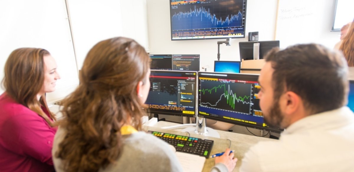 Three students working at a Bloomberg terminal in a classroom Three students working at a Bloomberg terminal in a classroom