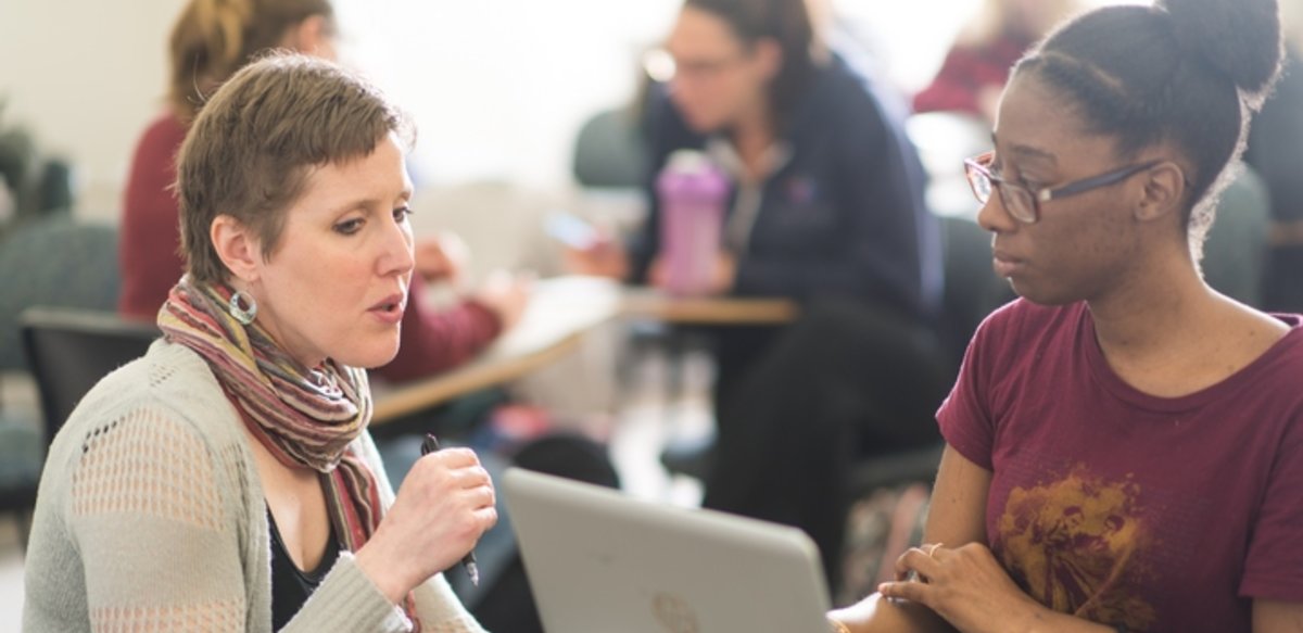 Professor speaking to a student at the student's desk and computer Professor speaking to a student at the student's desk and computer