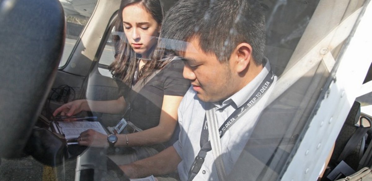 Two people in the cockpit of a plane reviewing paperwork. One person is wearing a lanyard that says Step to Delta. Two people in the cockpit of a plane reviewing paperwork. One person is wearing a lanyard that says Step to Delta.