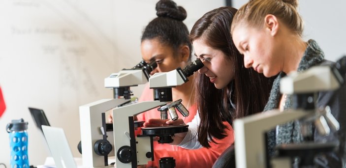 Three students using microscopes in geology lab