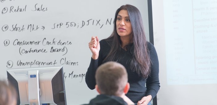 Professor Madhavi Venkatesan teaching class in front of a white board and projection screen Professor Madhavi Venkatesan teaching class in front of a white board and projection screen