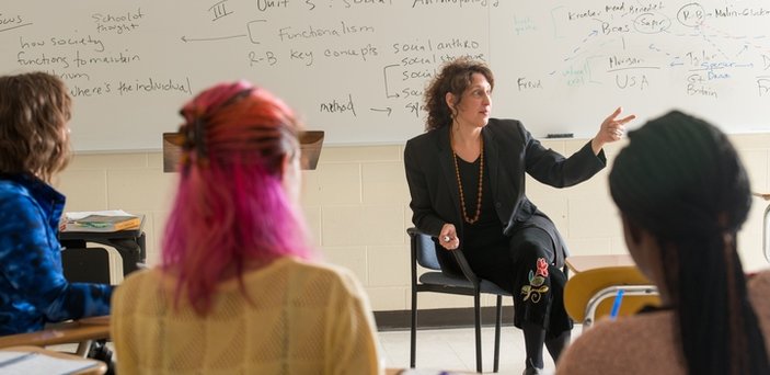 Professor Diana Fox teaching class sitting in front of a white board with notes about Unit 3: Social Anthropology