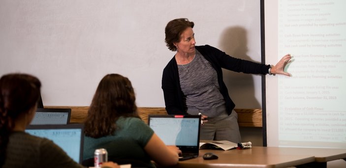 A professor teaching class pointing to content on a projector screen
