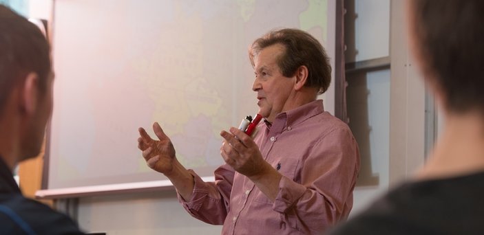 Professor Vernon Domingo teaching in front of large screen with a map on it