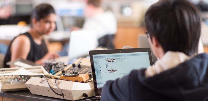 Students working on computers with electronic equipment on the table around them.