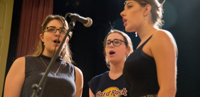 Three student singers standing around a microphone singing.