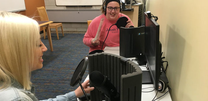 Two students laugh as they work together to record audio in the podcast studio.