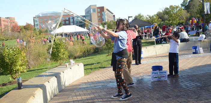 children creating huge bubbles with Homecoming Fair in background