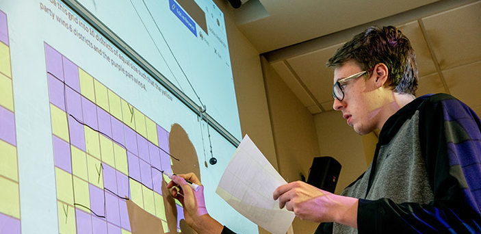 A BSU student at a white board dividing a grid into districts in a Math and Politics class