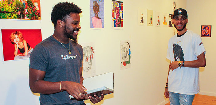 2 BSU students stand in front of their exhibits smiling in the Wallace Anderson Art Gallery on campus