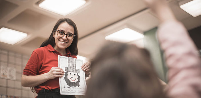 BSU student teacher smiling and holding up a childlike drawing of Abraham Lincoln while a student raises her hand