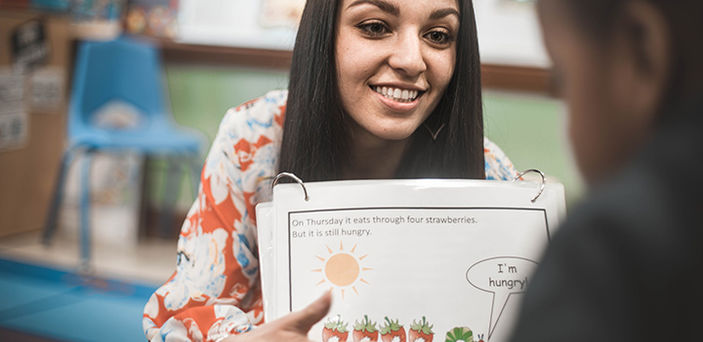 BSU student teacher working with a young student on reading with a flip chart