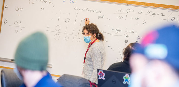 Dr. Margaret Black teaching class and writing on a white board with notes about A, B and "sum-of-products" with zeros and ones under it