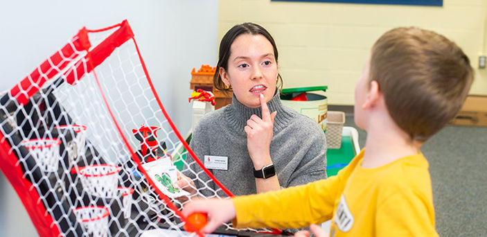 BSU student demonstrating to a young boy how to make a sound with her mouth to say a word