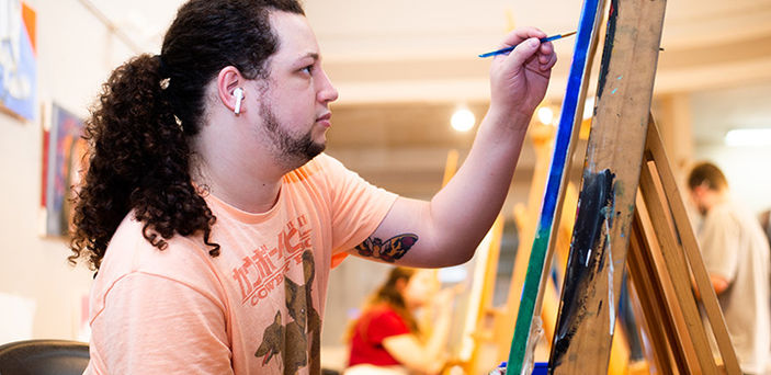 a BSU student painting at an easel with other students painting in the background