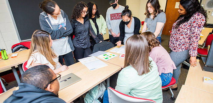 Professor Alice Cheng leaning over a classroom table showing materials to students who are gathered around the table