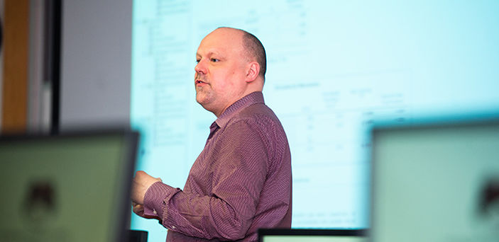 Professor Brian Frederick teaching in front of a projector screen