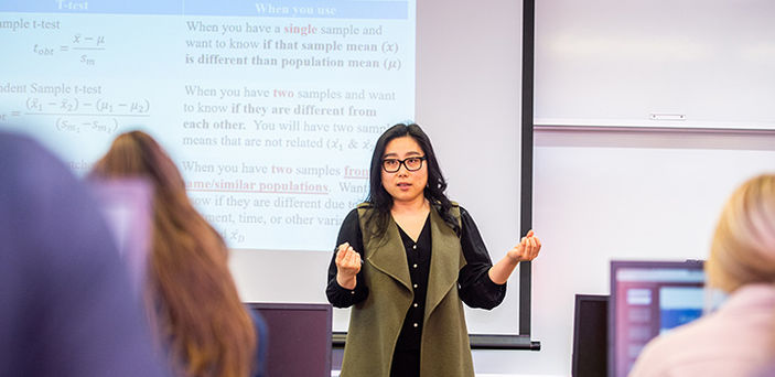 Professor Hannarae Lee teaching a class on Analyzing Criminal Justice Data speaking in front of a projector screen with notes about a T-test