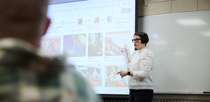 Dr. Melanie McNaughton points at images on a projector screen while teaching class